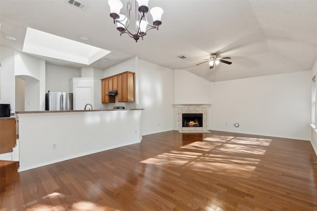 unfurnished living room with ceiling fan with notable chandelier, dark hardwood / wood-style flooring, lofted ceiling with skylight, and a tiled fireplace