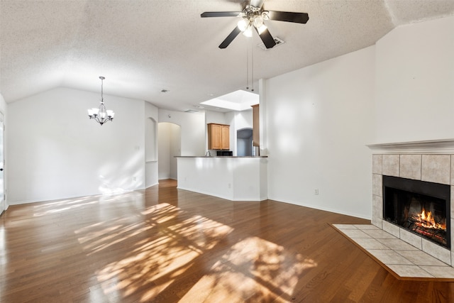 unfurnished living room featuring dark hardwood / wood-style flooring, a textured ceiling, ceiling fan with notable chandelier, vaulted ceiling, and a tile fireplace