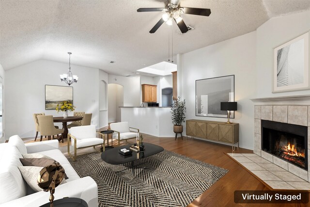 living room featuring ceiling fan with notable chandelier, vaulted ceiling, light wood-type flooring, a textured ceiling, and a fireplace