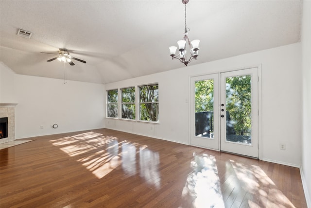 unfurnished living room featuring a tile fireplace, french doors, ceiling fan with notable chandelier, vaulted ceiling, and dark hardwood / wood-style floors