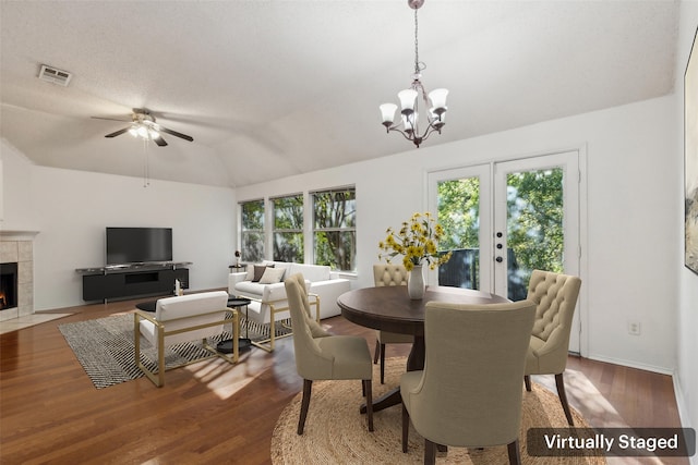 dining area with dark hardwood / wood-style flooring, vaulted ceiling, a healthy amount of sunlight, and a tiled fireplace