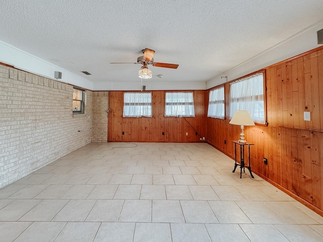 unfurnished room with a textured ceiling, ceiling fan, wood walls, and brick wall