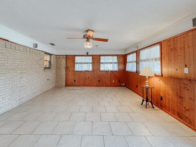 empty room featuring a textured ceiling, ceiling fan, and wood walls