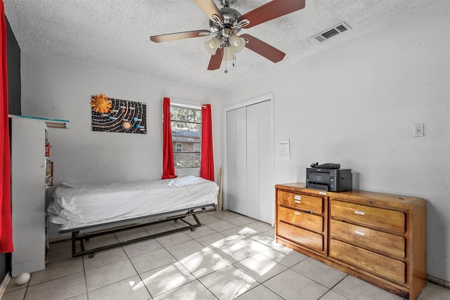 bedroom with ceiling fan, light tile patterned floors, a textured ceiling, and a closet