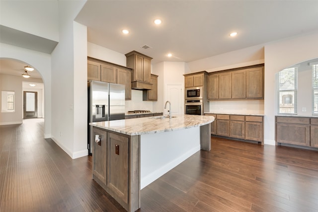 kitchen with dark wood-type flooring, stainless steel appliances, a center island with sink, and sink