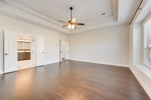 empty room with dark hardwood / wood-style flooring, a tray ceiling, and ceiling fan