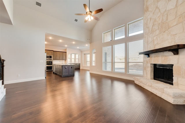 unfurnished living room featuring a fireplace, high vaulted ceiling, ceiling fan, and dark wood-type flooring