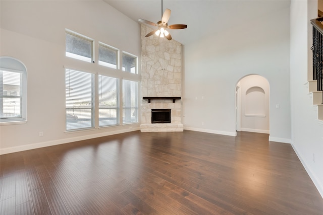 unfurnished living room featuring a stone fireplace, ceiling fan, high vaulted ceiling, and dark wood-type flooring