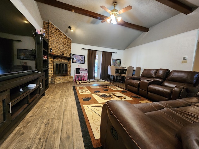 living room with ceiling fan, vaulted ceiling with beams, a textured ceiling, a fireplace, and hardwood / wood-style flooring