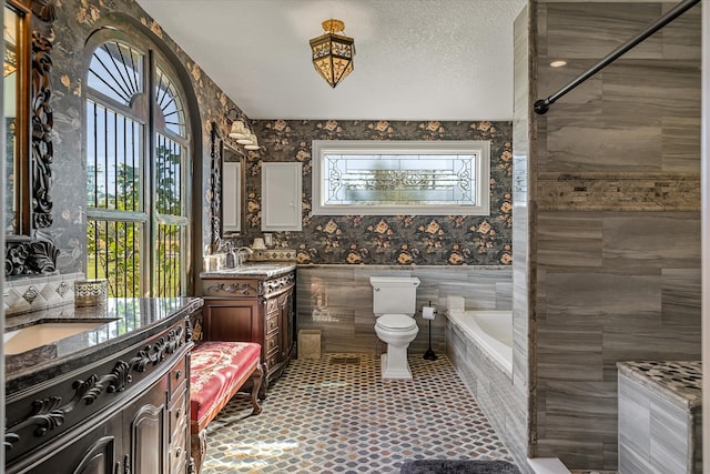 bathroom featuring vanity, toilet, a textured ceiling, tile walls, and tiled bath