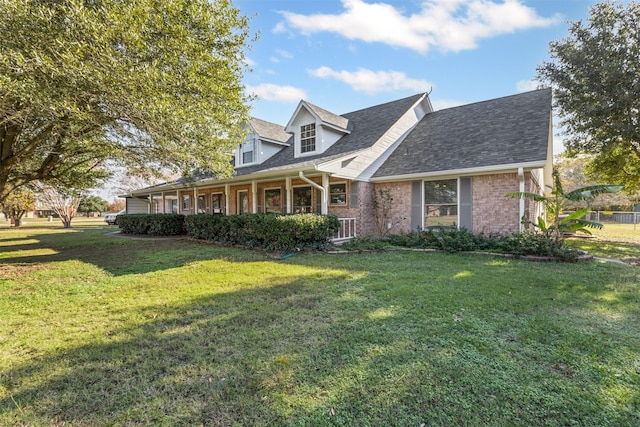 cape cod-style house featuring a front yard, covered porch, brick siding, and roof with shingles