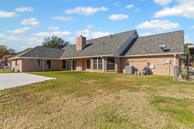 back of property with brick siding, a yard, a chimney, and roof with shingles