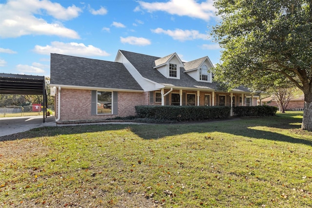 cape cod-style house featuring a shingled roof, a front yard, brick siding, and a detached carport