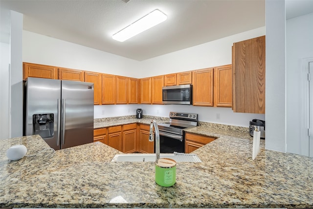 kitchen featuring kitchen peninsula, light stone countertops, sink, and stainless steel appliances