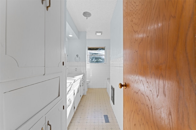 bathroom with a textured ceiling, vanity, tile walls, and toilet