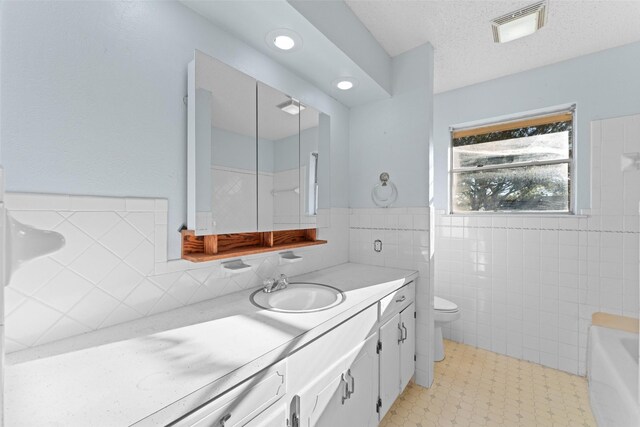 bathroom featuring a textured ceiling, vanity, toilet, and tile walls