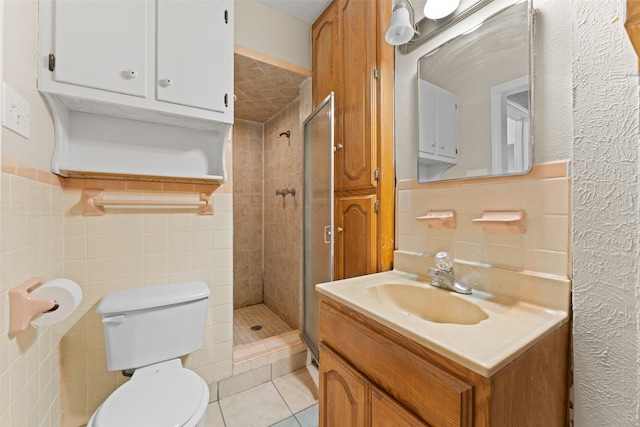 bathroom featuring tile patterned floors, toilet, tiled shower, vanity, and tile walls