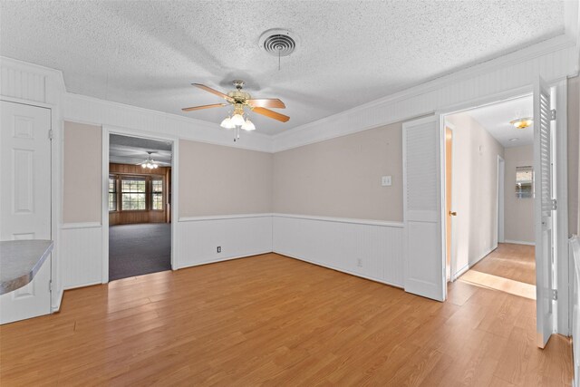 spare room with a textured ceiling, light wood-type flooring, ceiling fan, and crown molding