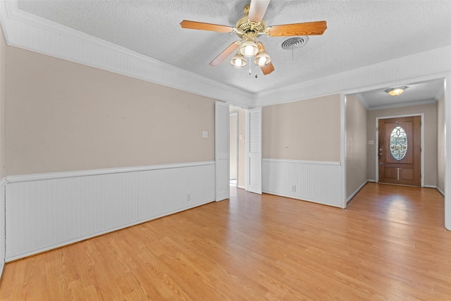 interior space with ceiling fan, light hardwood / wood-style floors, a textured ceiling, and ornamental molding