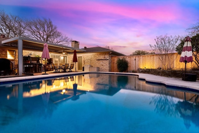 pool at dusk featuring area for grilling and a patio