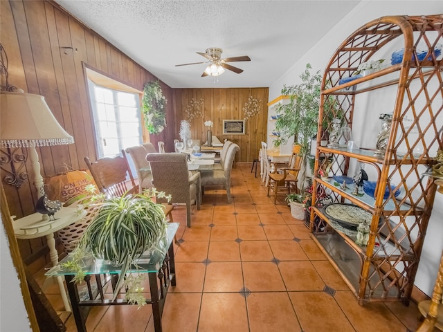 tiled dining area featuring ceiling fan, a textured ceiling, and wooden walls