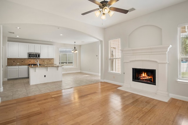 unfurnished living room with ceiling fan with notable chandelier, light hardwood / wood-style floors, a healthy amount of sunlight, and a tiled fireplace