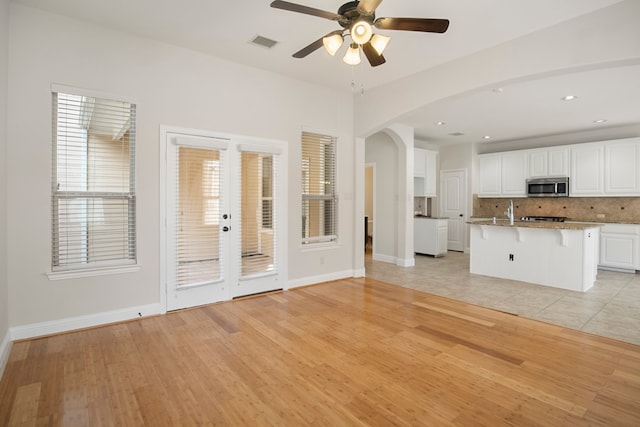 interior space with a kitchen bar, a kitchen island with sink, ceiling fan, light hardwood / wood-style flooring, and white cabinetry