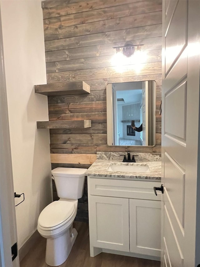 bathroom featuring hardwood / wood-style flooring, toilet, vanity, and wood walls