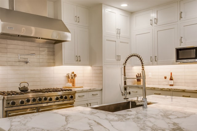 kitchen with white cabinets, appliances with stainless steel finishes, light stone counters, and wall chimney exhaust hood