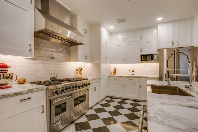 kitchen with white cabinets, wall chimney range hood, sink, decorative backsplash, and appliances with stainless steel finishes