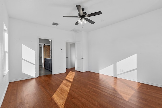 unfurnished bedroom featuring connected bathroom, ceiling fan, dark wood-type flooring, and a barn door