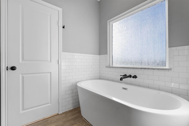 bathroom with a bathtub, wood-type flooring, and tile walls