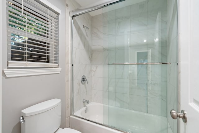 bathroom featuring toilet and shower / bath combination with glass door