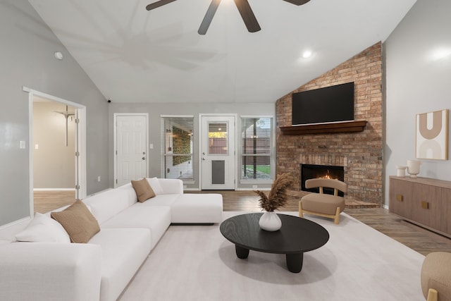 living room with ceiling fan, light hardwood / wood-style floors, lofted ceiling, and a brick fireplace