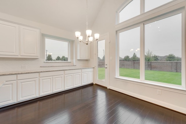 unfurnished dining area featuring vaulted ceiling, an inviting chandelier, and dark hardwood / wood-style flooring