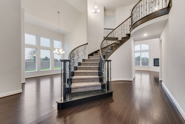 stairs with an inviting chandelier, a towering ceiling, a healthy amount of sunlight, and hardwood / wood-style flooring