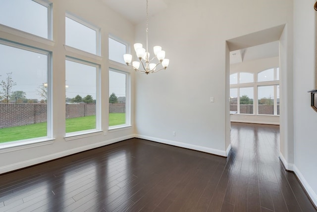 unfurnished dining area with a notable chandelier, dark hardwood / wood-style floors, and a high ceiling