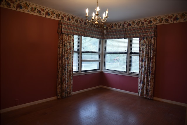 empty room featuring crown molding, hardwood / wood-style floors, a healthy amount of sunlight, and a notable chandelier