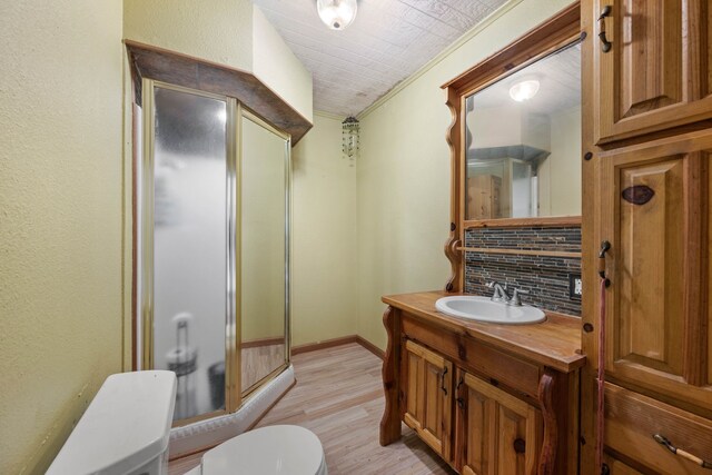 full bath featuring a stall shower, decorative backsplash, toilet, ornamental molding, and wood finished floors