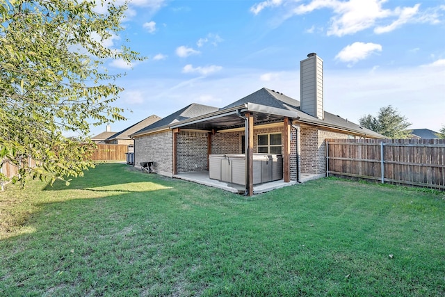 rear view of property featuring a patio, a hot tub, and a lawn