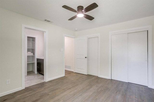 unfurnished bedroom with ceiling fan, light hardwood / wood-style floors, multiple closets, and ensuite bath