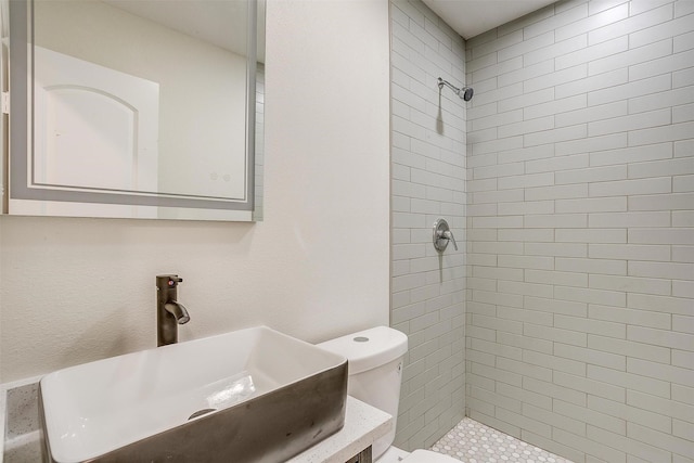 bathroom with tiled shower, vanity, and toilet