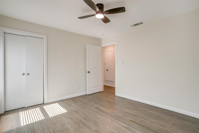 unfurnished bedroom featuring baseboards, visible vents, ceiling fan, wood finished floors, and a closet