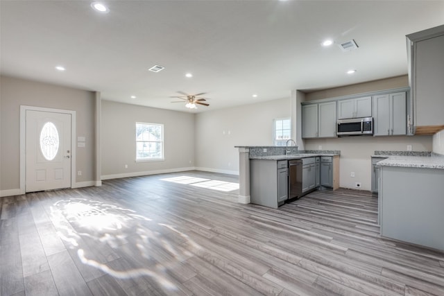 kitchen with gray cabinets, stainless steel appliances, light wood-type flooring, light stone countertops, and ceiling fan