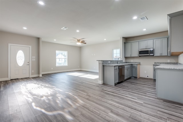 kitchen featuring light stone countertops, stainless steel appliances, light hardwood / wood-style floors, gray cabinets, and ceiling fan