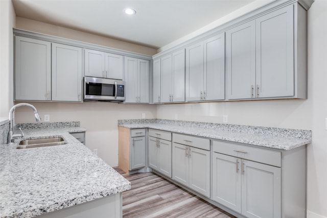 kitchen with sink, light wood-type flooring, light stone counters, and gray cabinets