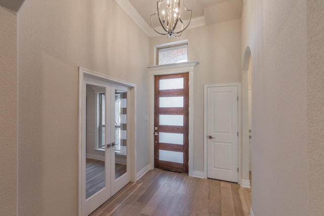 entrance foyer featuring french doors, ornamental molding, hardwood / wood-style flooring, a chandelier, and a high ceiling