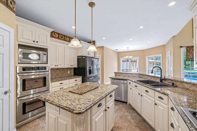 kitchen featuring white cabinetry, sink, decorative light fixtures, a kitchen island, and appliances with stainless steel finishes