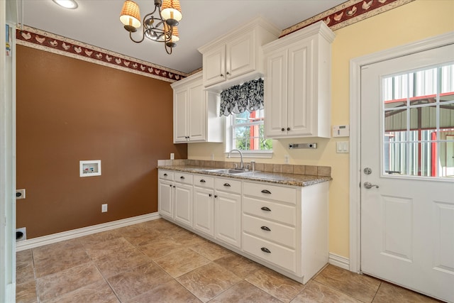 kitchen featuring white cabinets, light stone counters, sink, and a chandelier