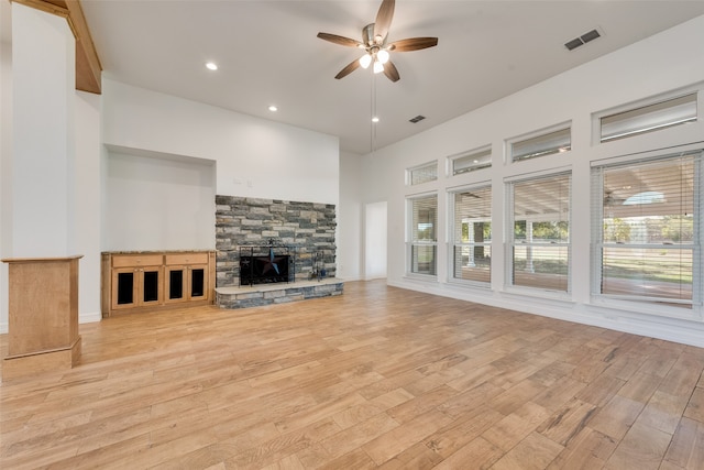 unfurnished living room with a stone fireplace, ceiling fan, light hardwood / wood-style floors, and a high ceiling